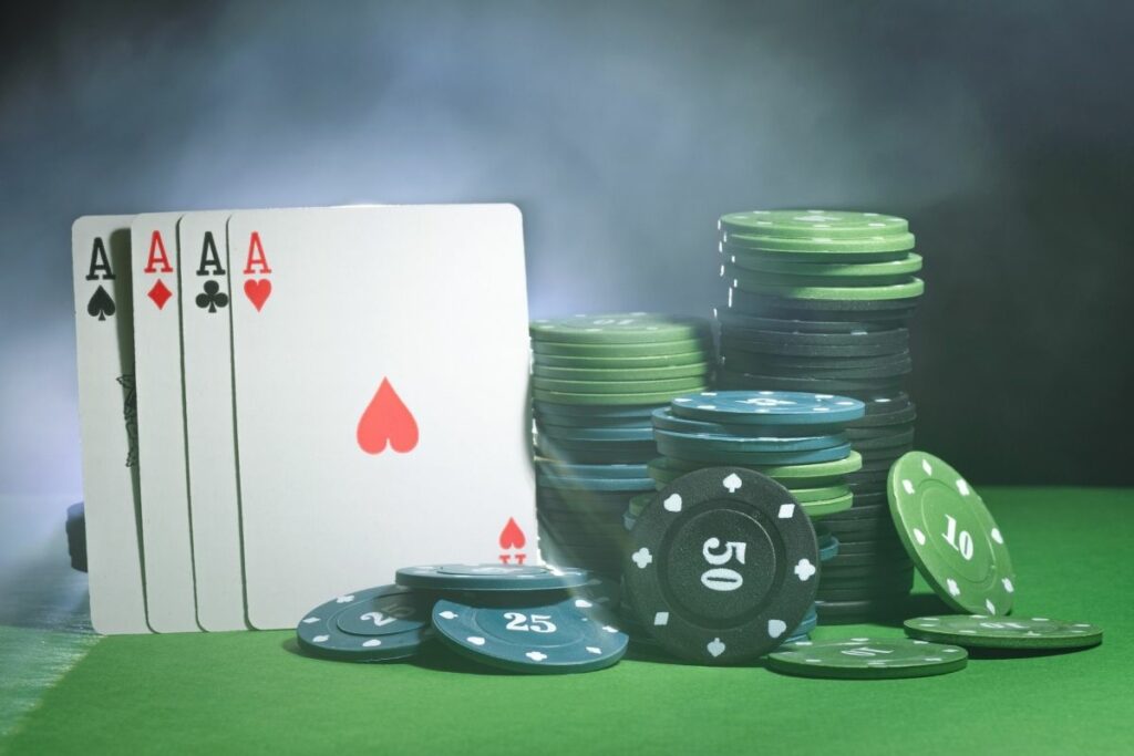 four aces cards and poker chips in the smoke on the green table background