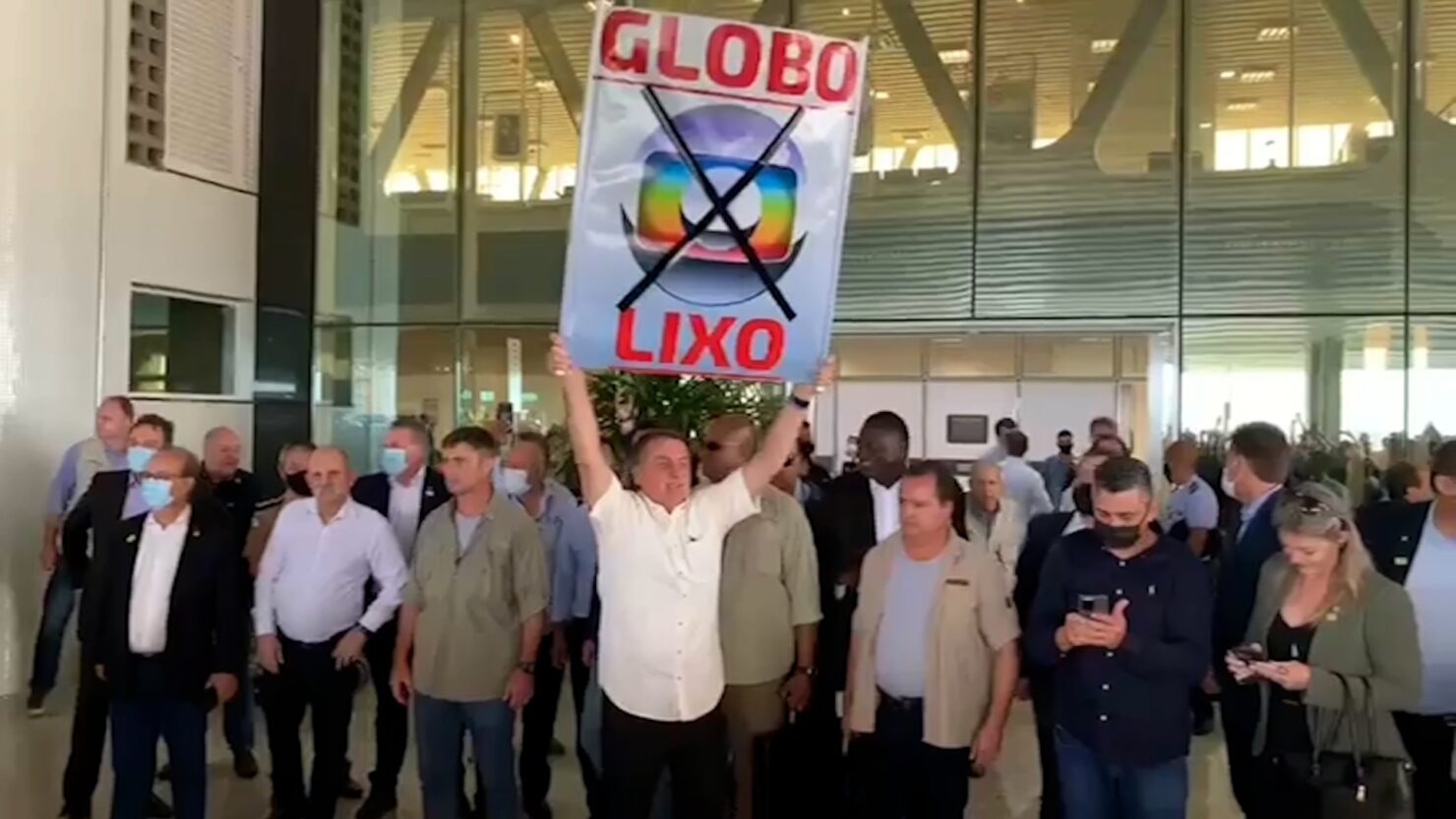 Bolsonaro estendendo cartaz de Globo Lixo em aeroporto ec1aB9